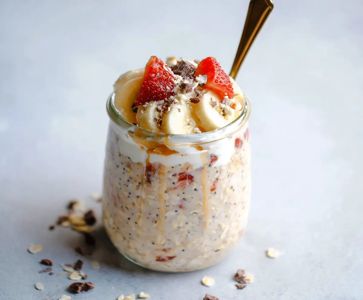 Creamy banana split overnight oats topped with fresh strawberries and chocolate drizzle in a glass jar.