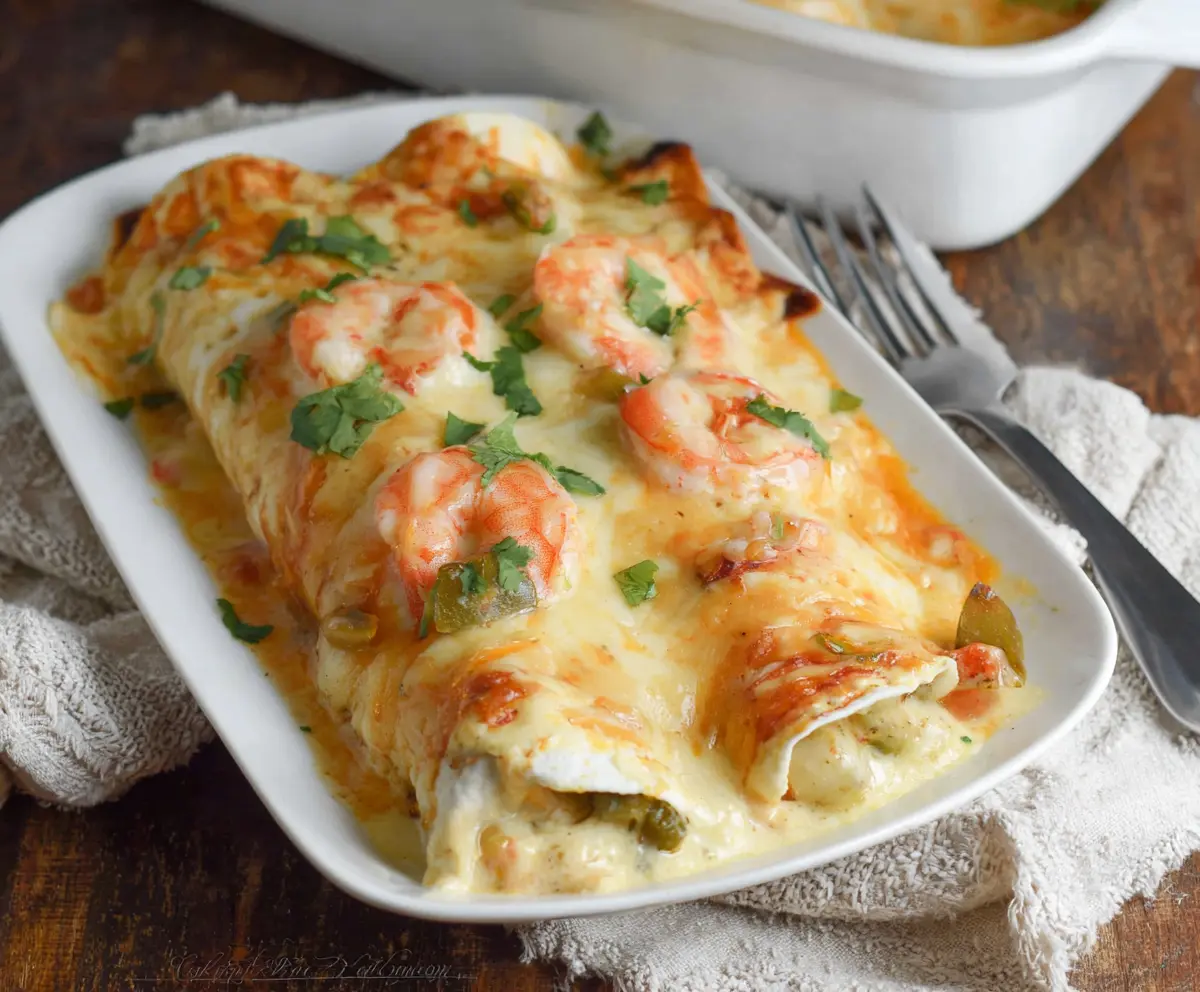 Delicious creamy shrimp enchiladas topped with melted cheese and fresh cilantro on a plate.