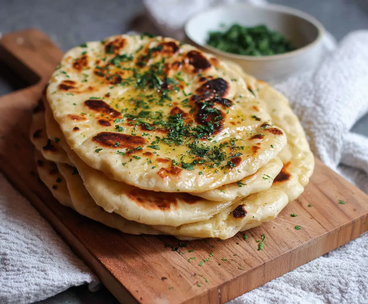 Homemade sourdough discard naan bread on a wooden board, showcasing fluffy and golden baked Indian flatbread.