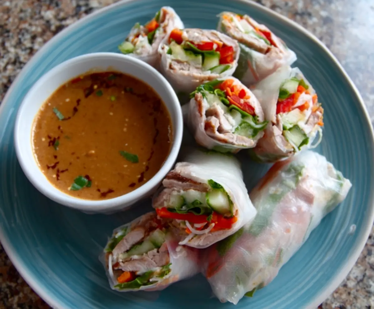Delicious pork spring rolls served with a tangy peanut lime sauce on a plate.